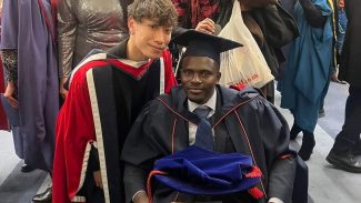 Graduates wearing gown and caps smile with friends and family around.