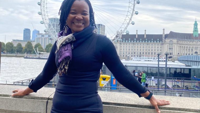 A woman smiling and leaning with the London eye behind her